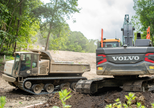 A dumptruck and a large earth mover in the woods. Brex company sets new standards in all aspects of construction